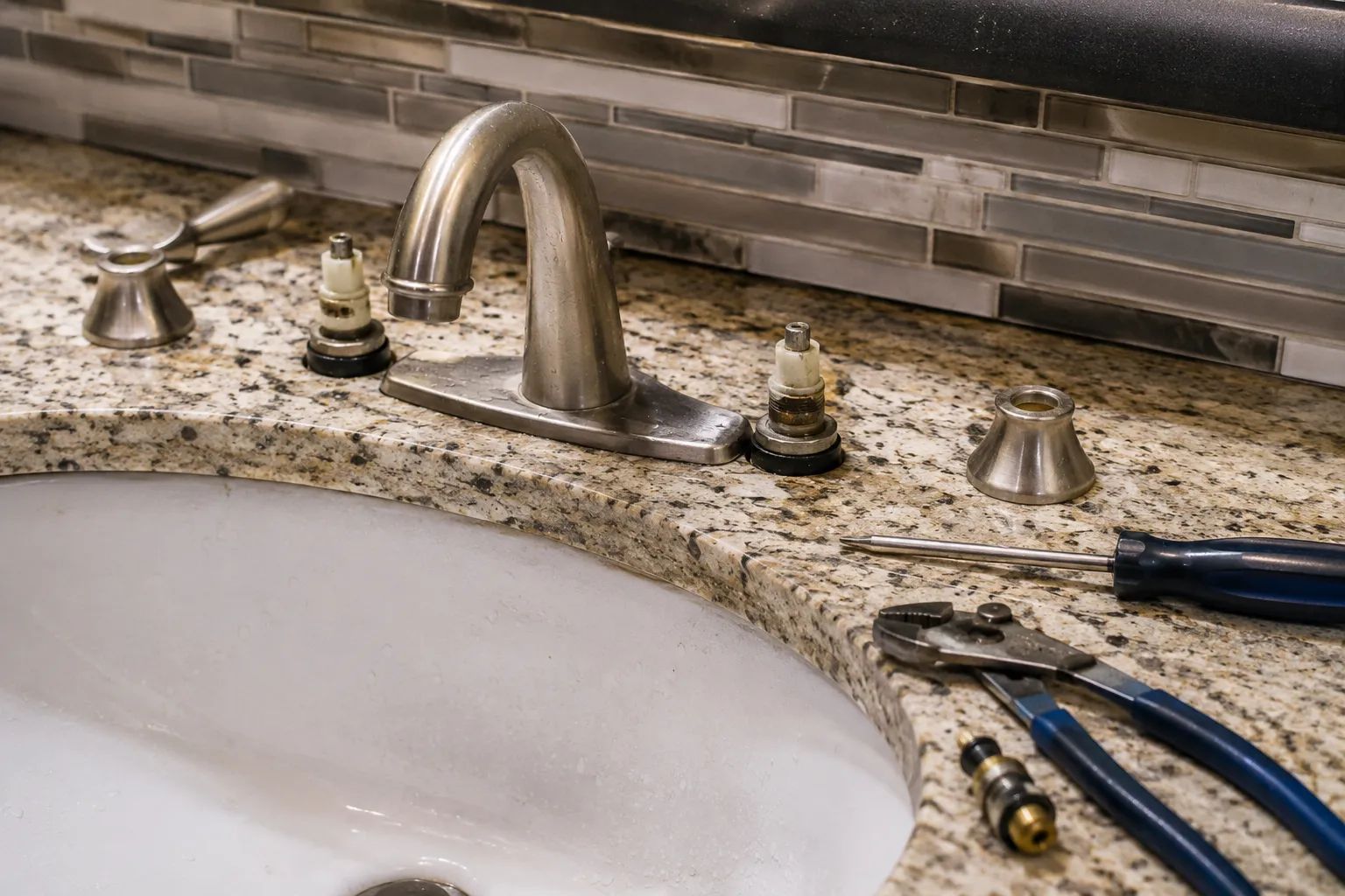 Disassembled bathroom faucet with exposed valve components and repair tools on the countertop.