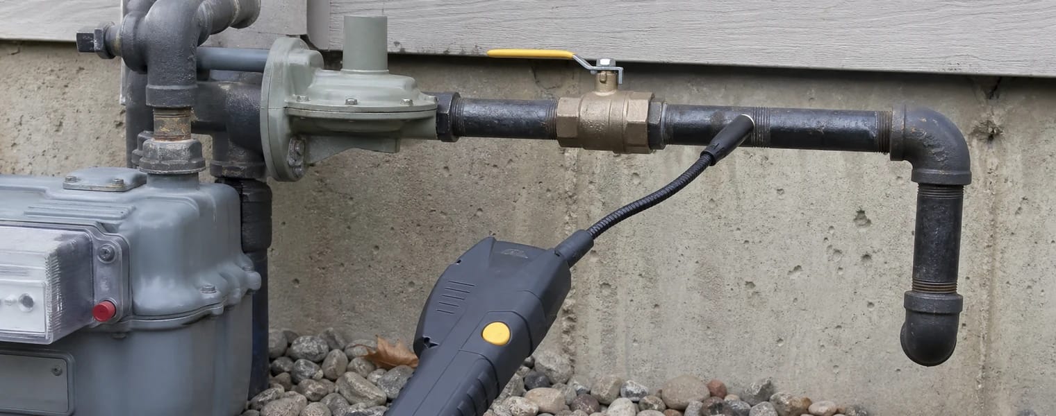 Close-up of a residential gas shut-off valve beside an electronic leak detector.
